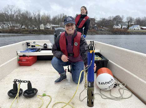 Two women on the deck of a boat with water quality measuring equipment